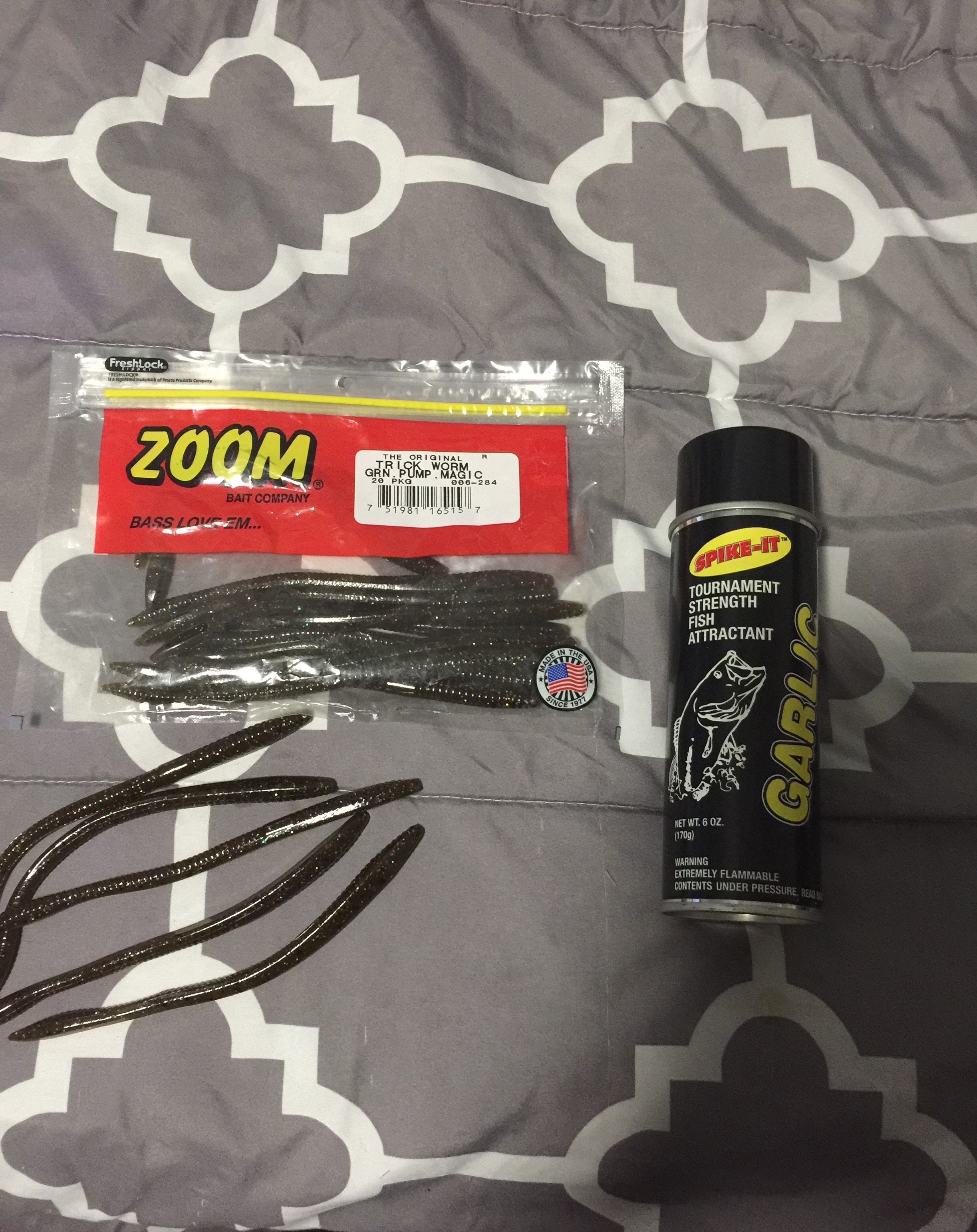 In this picture is my bed spread and on top of the bed spread is a package of fake worms with a can of garlic spray beside the worms. 